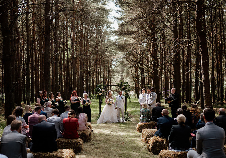 Woodland ceremony with guests sitting on bales of hay